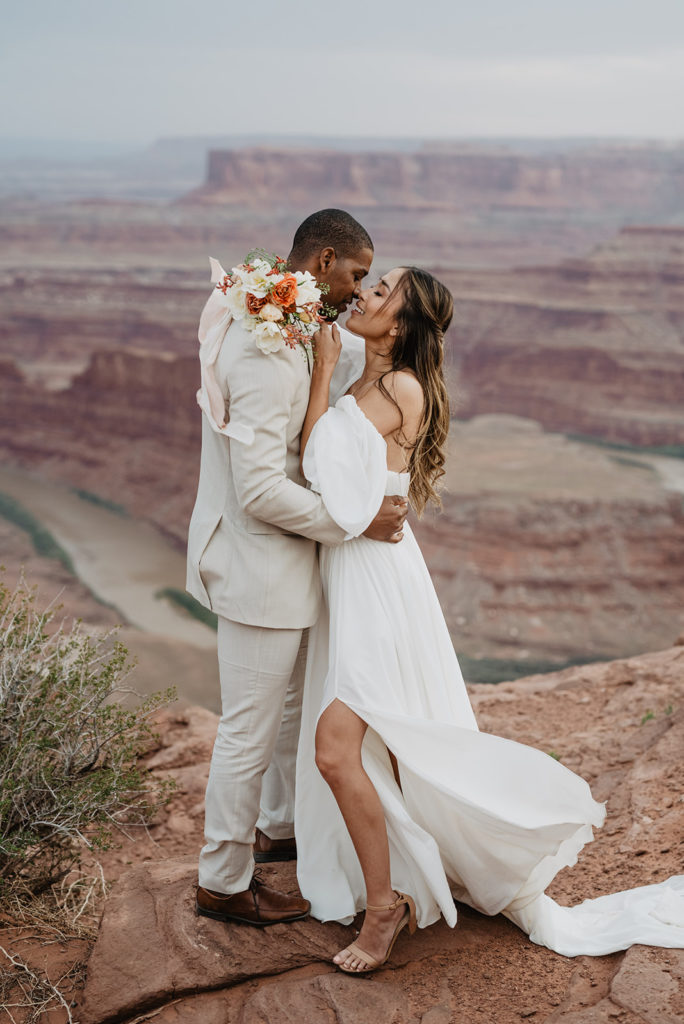 wedding day first look alternatives with bride and groom kissing on a mountain top at their Arches national park wedding day with the canyon and red rocks in the distance captured by Utah elopement photographer