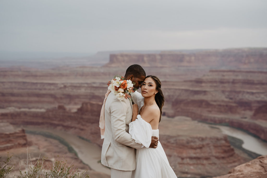 bride and groom embracing each other at their Arches National Park wedding on top of a boulder with a valley below them captured by Utah Elopement Photographer