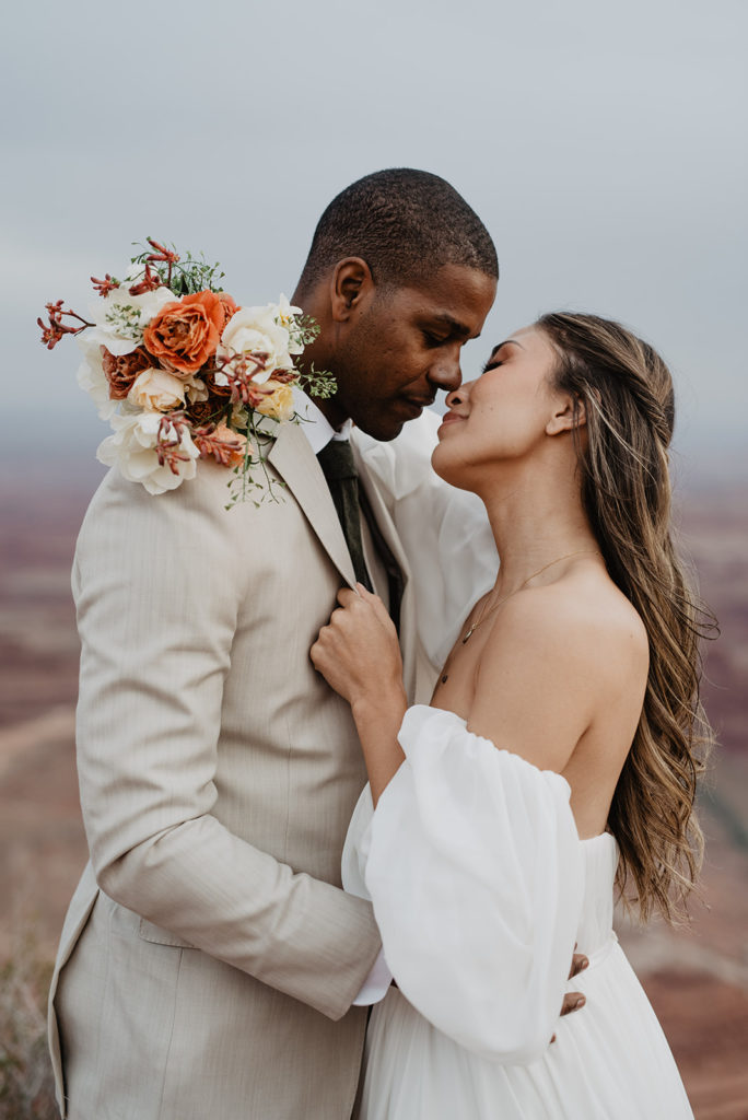 bride leans into her groom and holds onto his lapels while looking up to kiss him while holding an orange wedding bouquet over her shoulder captured by Utah elopement photographer