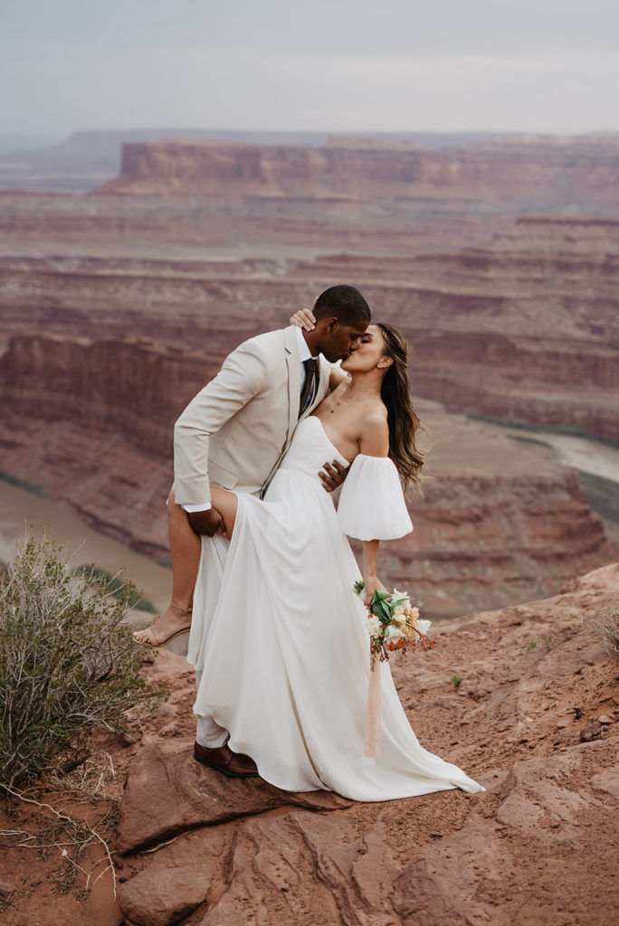 groom holds his brides leg as he dips her backwards and kisses her passionately at Arches National Park wedding photographed by Utah Elopement Photographer