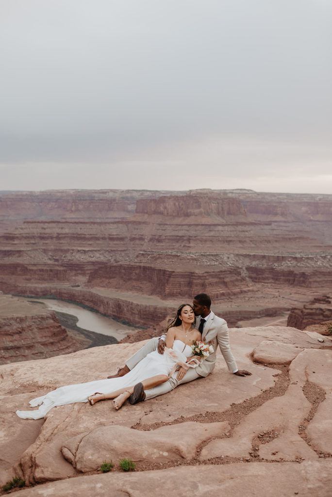 Arches National Park wedding photographed by Utah elopement photographer with bride and groom sitting together on an outlook in the canyon
