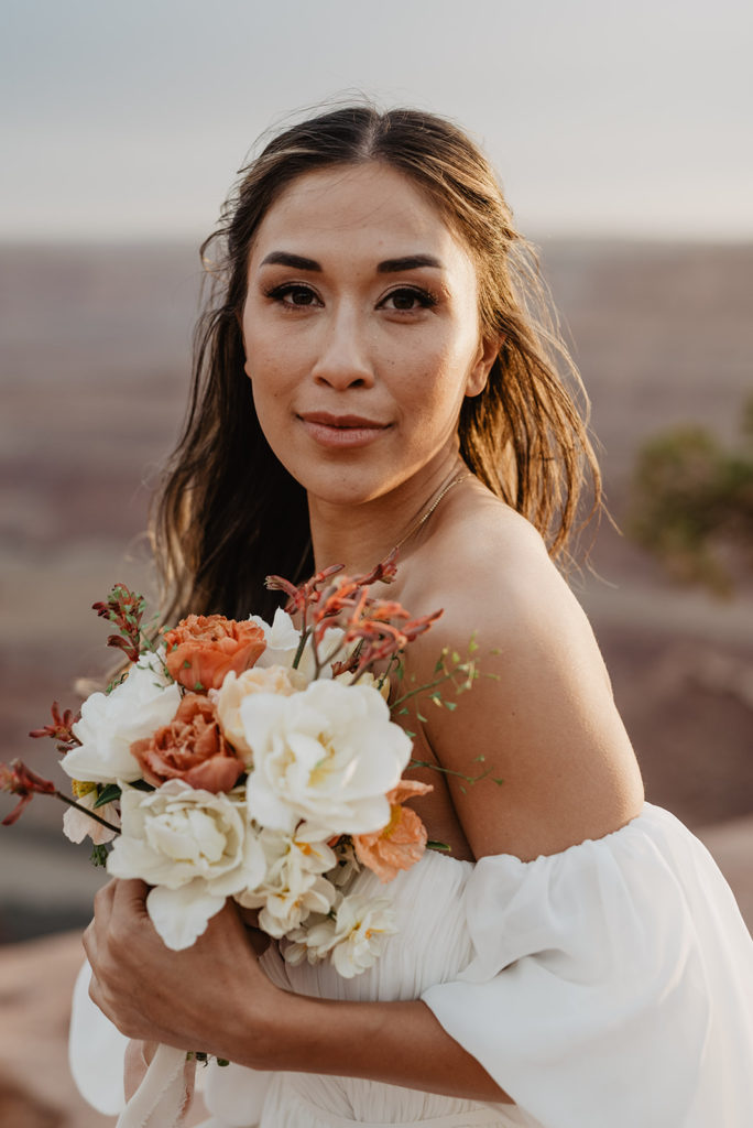 bride holding her small floral bouquet up to her face and smiling during her Arches National Park wedding 