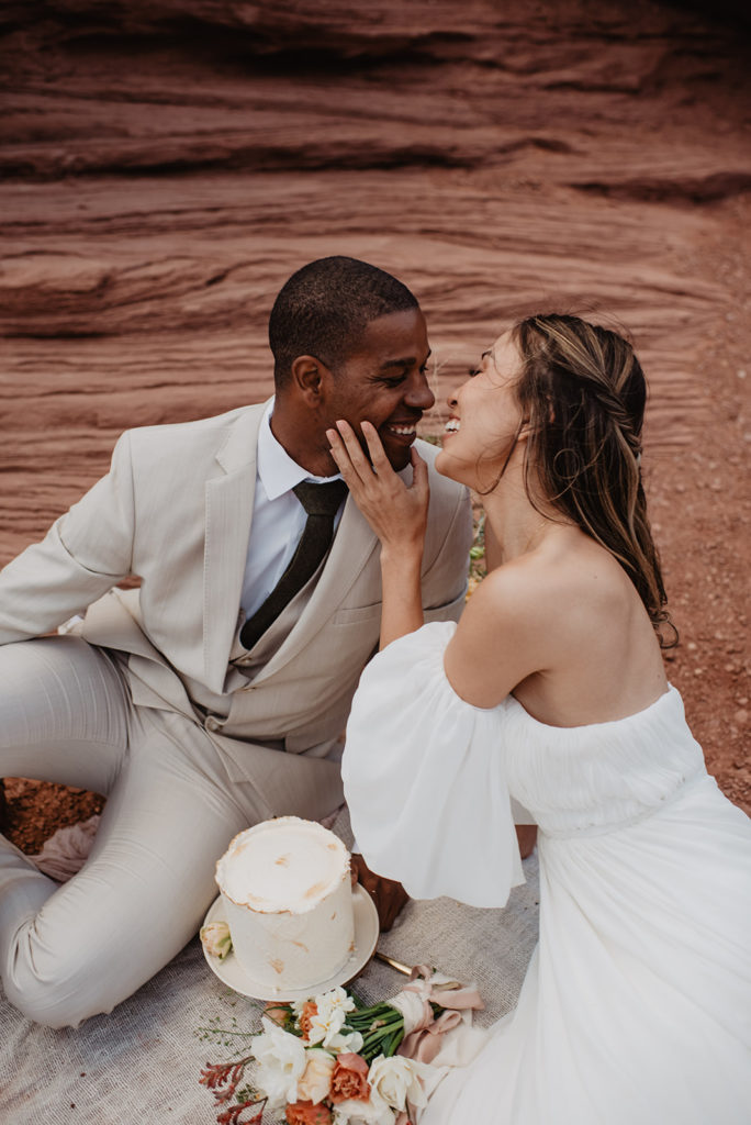 Utah elopement photographer captures bride and groom kissing before they cut into a cake they have for a picnic celebration for their Arches National Park wedding 