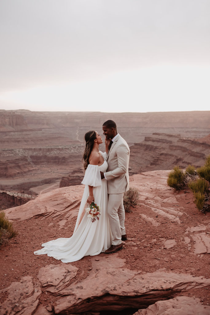 utah elopement photographer captures bride and groom embracing on a mountain top in Moab for their Arches National Park wedding 