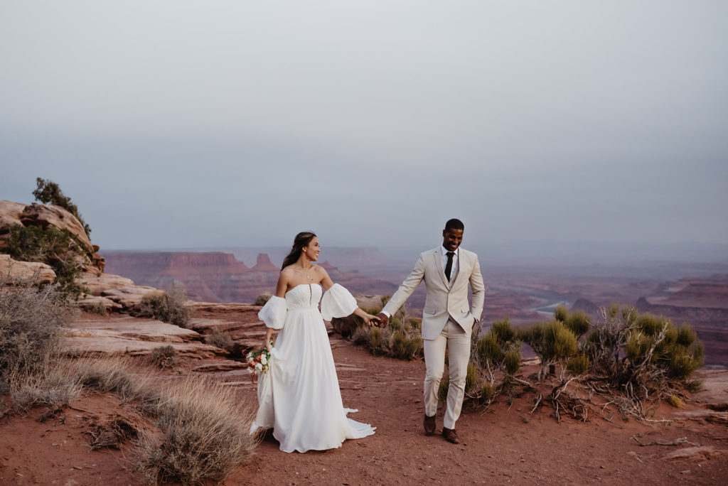 Arches National Park wedding with bride and groom on top of a mountain together holding hands and looking at one another after the sunset with Utah elopement photographer 