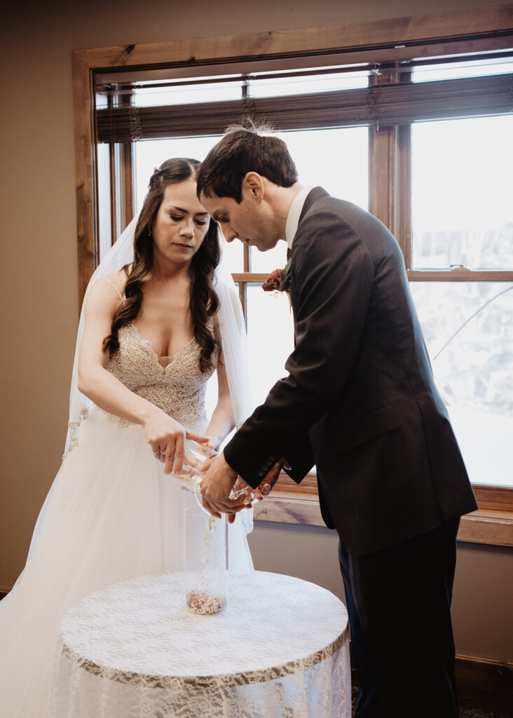 jackson hold wedding photographers photographs bride in a lace beaded wedding dress pouring sand into a vase with her groom for their indoor wedding ceremony