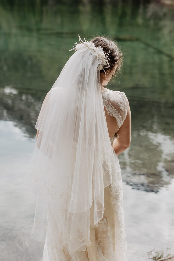 bridal portrait by jackson hole photographers with detail shot of brides veil as she stands on a rock in a river for her wyoming elopement