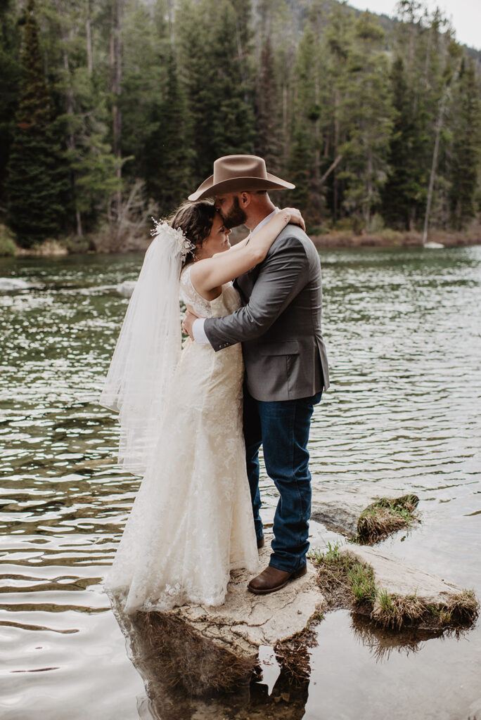groom kissing his bride on the forehead as he hugs her in a river bed for their grand teton wedding