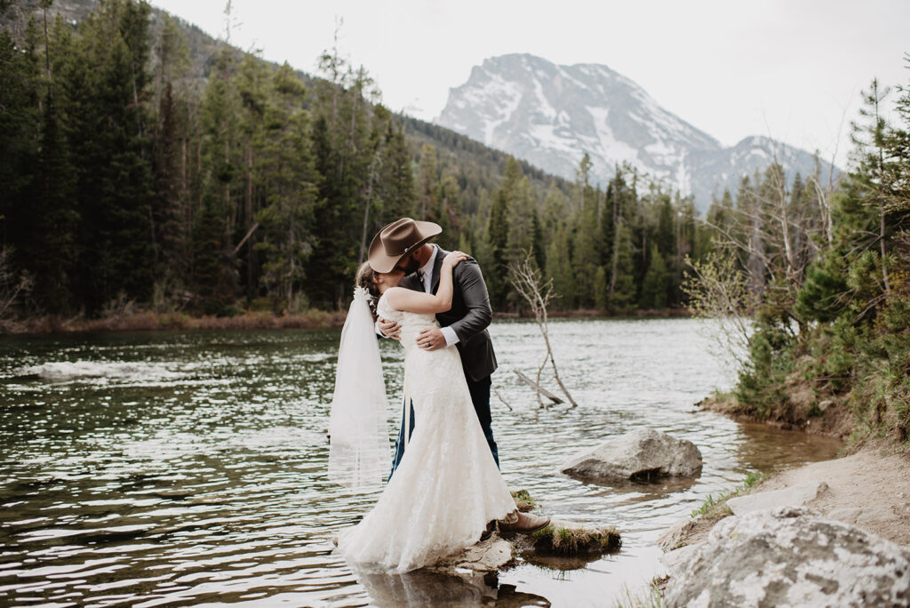 outdoor wedding pictures for a wyoming elopement with jackson hole photographers with bride and groom on a rock in the river with the groom dipping back the bride a bit and kissing her as he holds her waist