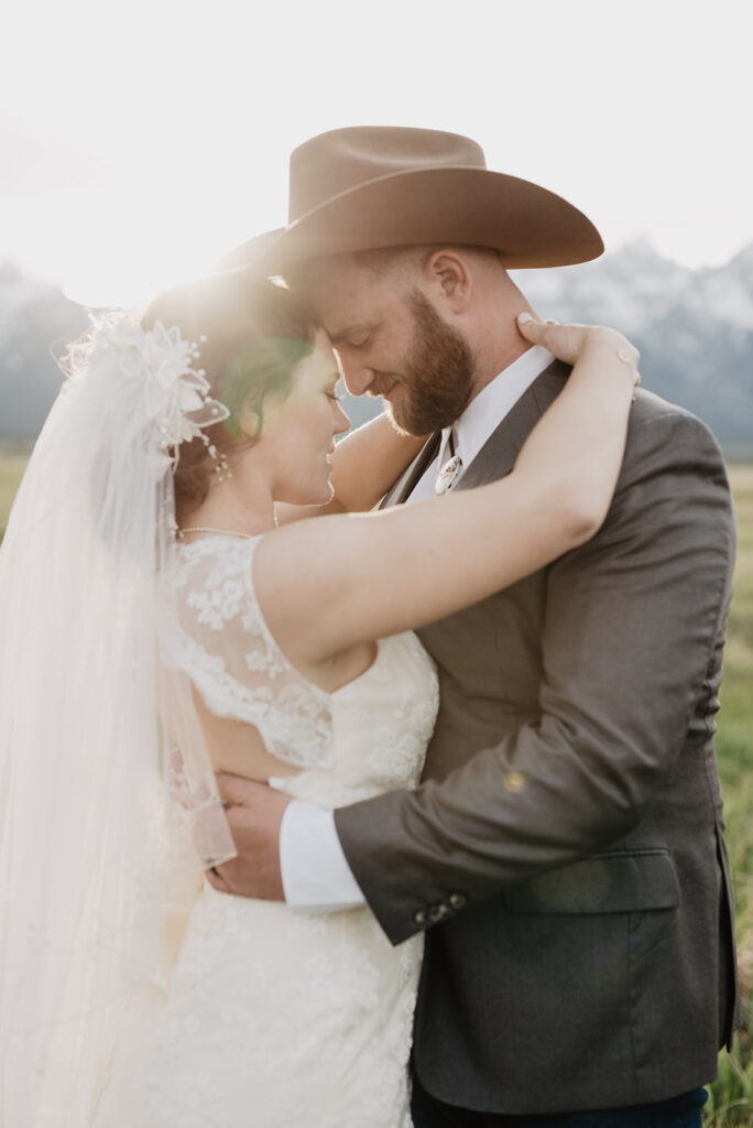 jackson hole photographers photographs bride holding her arms around her grooms neck and resting her forehead on his as they embrace for their grand teton wedding pictures
