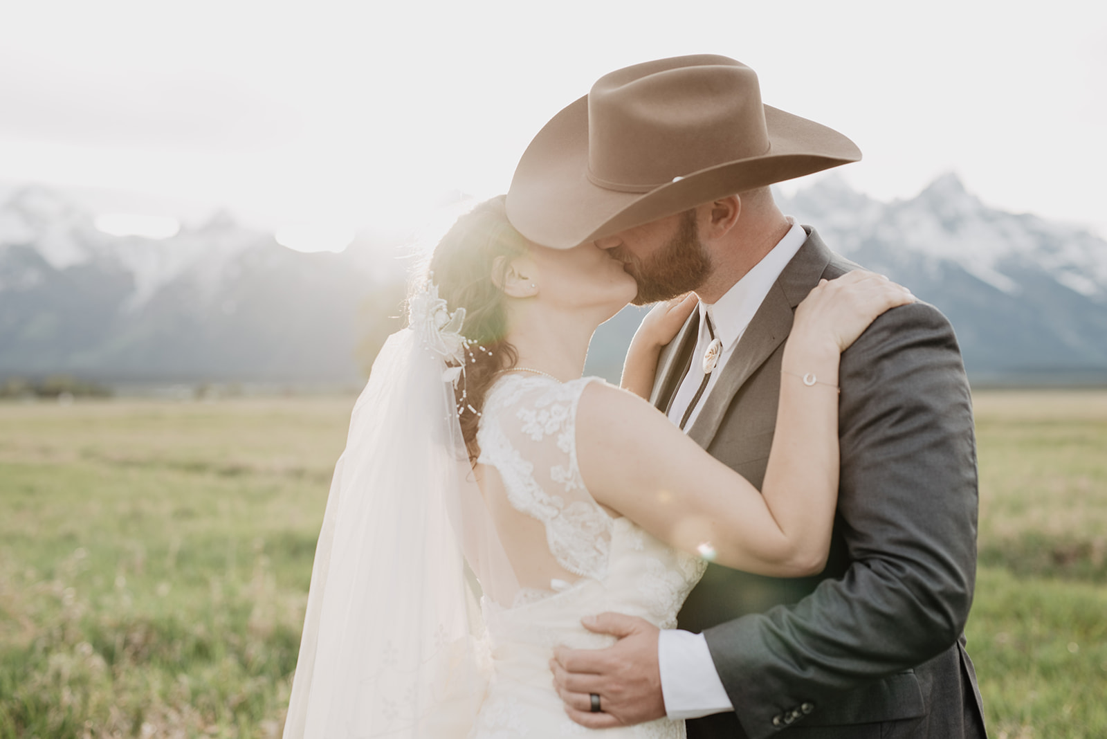 jackson hole photographers captures romantic wedding pictures in Grand Tetons with bride and groom kissing as the sun shines over the mountains in the distance