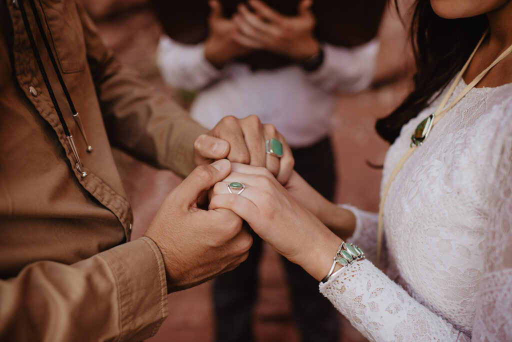 detail shot with bride and groom holding holds at their outdoor wedding ceremony in arches national park with their turquoise wedding rings captured by utah elopement photographer