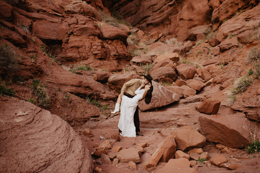 groom dipping his bride back and kissing her passionately in the red rocks of southern utah for their destination elopement with utah elopement photographer