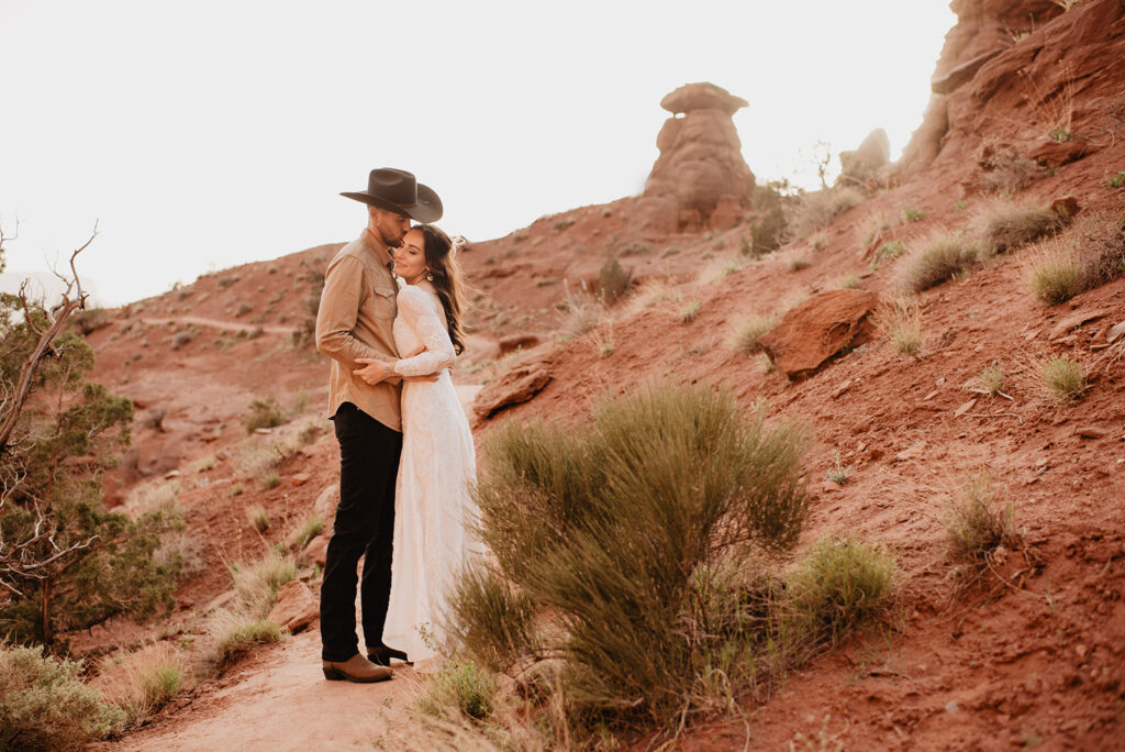 Moab elopement with bride and groom on a trail in the red rocks hugging on another and laughing with rock formations in the distance