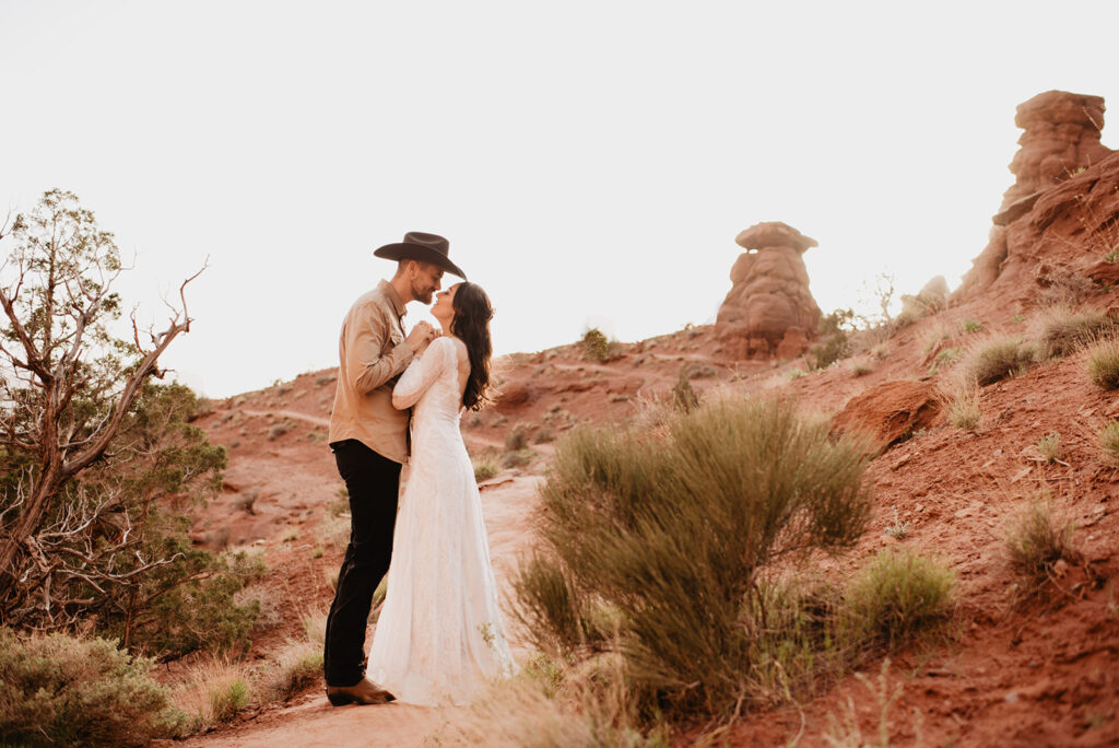 utah elopement photographer captures bride and groom holding hands together to their chests as they lean into each other to kiss with the red rocks of Arches National Park