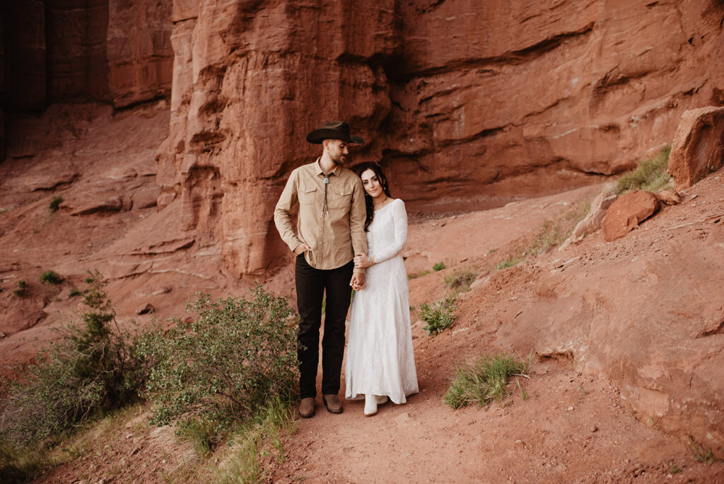 Utah Elopement Photographer captures groom wearing cowboy hat and bride leaning against him during bridal portraits after Moab Elopement