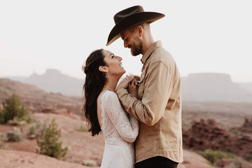 utah elopement photographer photographs utah elopement with bride and groom holding hands and laughing with one another as they stand on a mountain in arches national park
