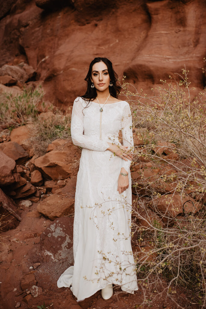 utah elopement photographer captures bride in a lace dress posing in the red rocks of arches national park in the brush for her utah elopement 