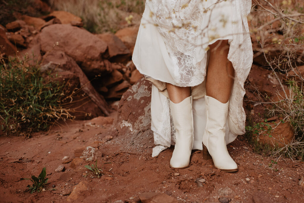 bride wearing white cowboy boots as she walking through the red rocks of arches national park for her utah elopement 