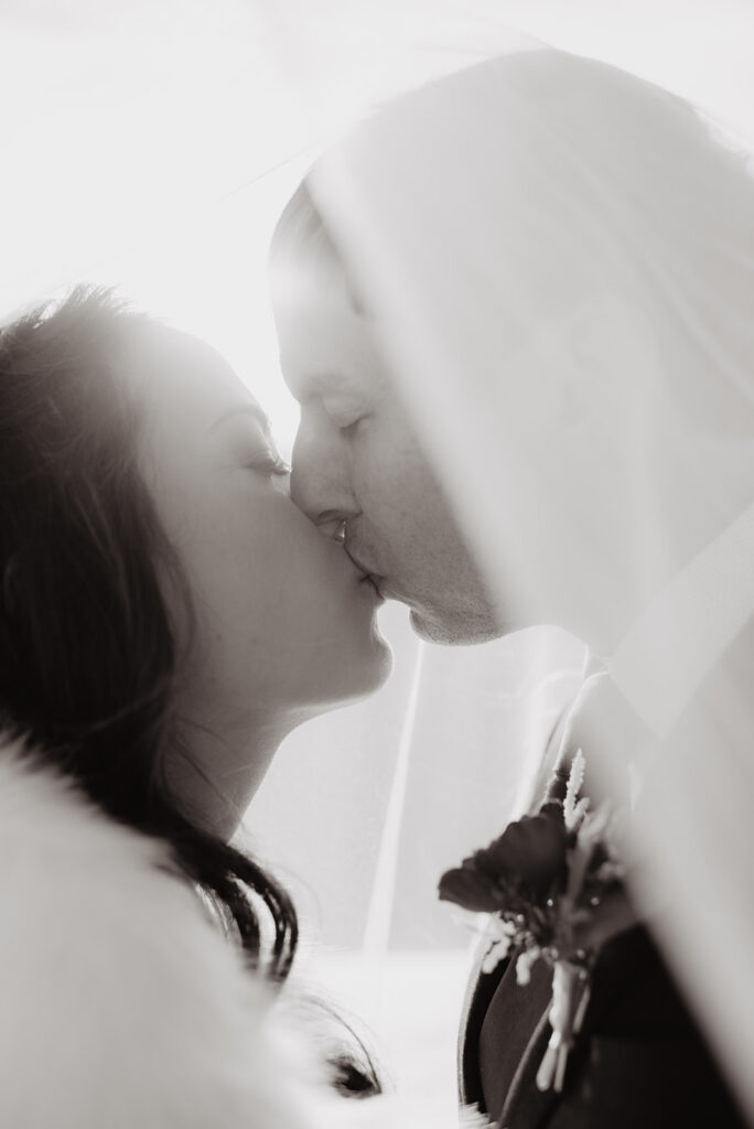 Grand Teton Photographer captures black and white portrait of couple kissing under veil after Grand Teton wedding