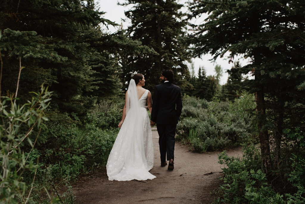 Jackson Hole wedding photographer captures bride and groom walking into forest