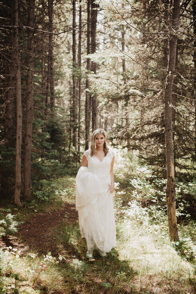 Jackson Wy photographer captures bride holding wearing dress walking through forest