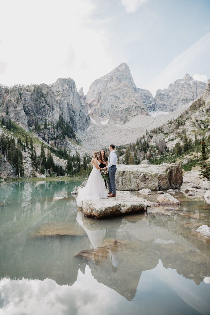 Jackson Wy photographer captures bride and groom holding hands on rock during wedding ceremony in Grand Teton National Park