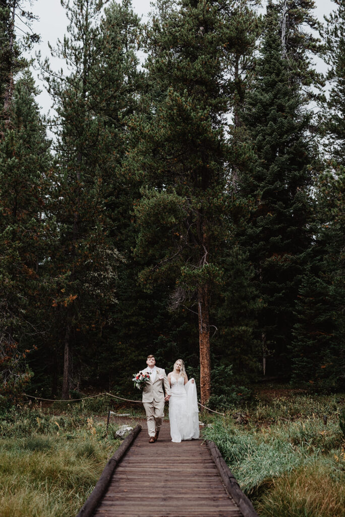 Jackson Hole Wedding Photographer captures bride and groom holding hands walking into forest