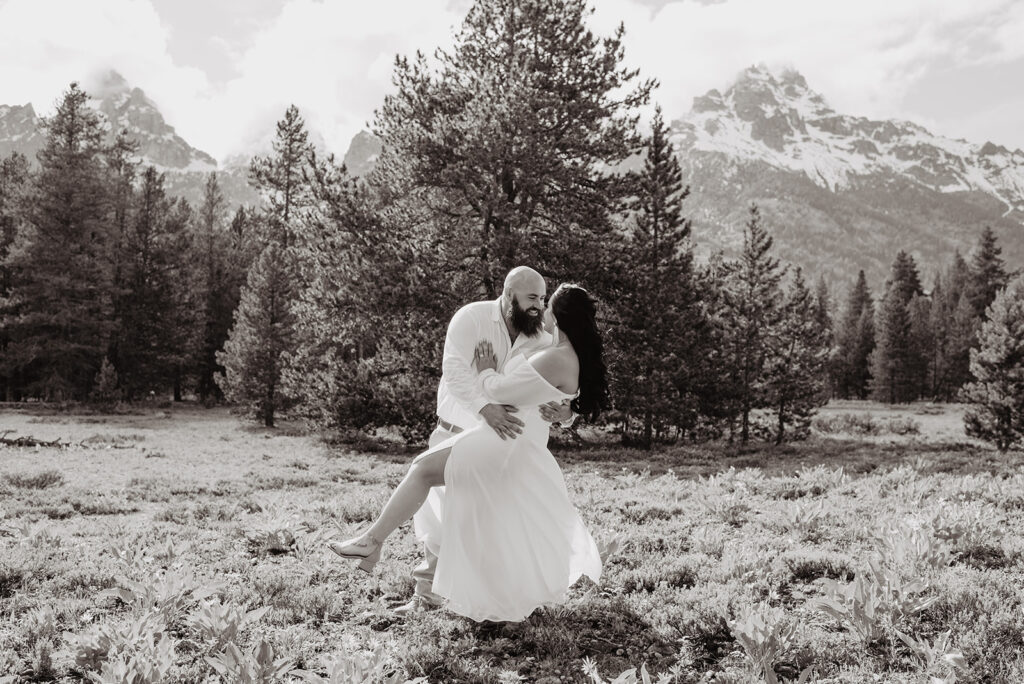 black and white elopement picture by jackson hole photographer with groom dancing and dipping his bride backwards with the Grand Tetons in the distance 