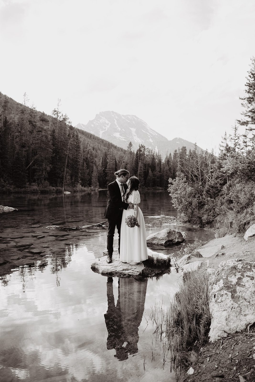 black and white wedding photo with bride and groom standing on a rock in a lake and embracing