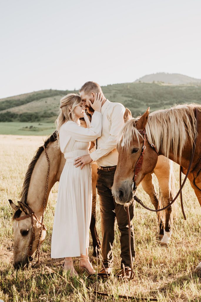 Jackson Hole photographer photographs bride holding her grooms face to hers as they rest their foreheads together while standing in a pasture with their horses