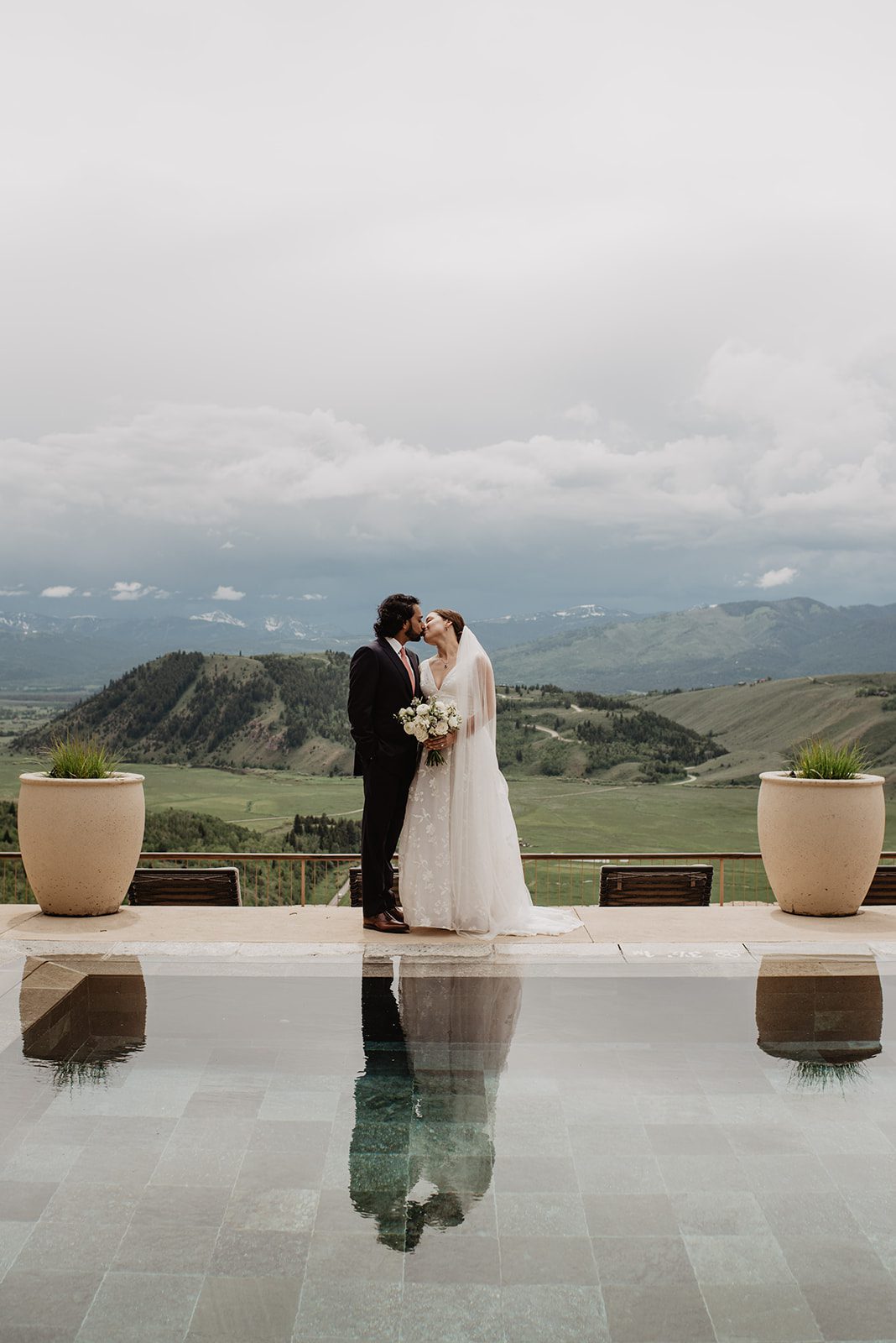 Amangani Resort Jackson Hole wedding with bride and groom kissing one another with the pool below them showing their reflection with the hills and mountains of the tetons in the distance