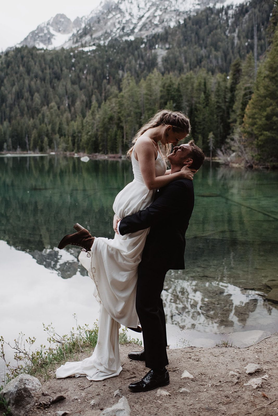 A romantic lift captured by the emerald waters of String Lake, with towering evergreens and snow-capped peaks as a backdrop. This tender moment, photographed by a Jackson Hole photographer, perfectly reflects the adventurous spirit of the couple's mountain elopement.